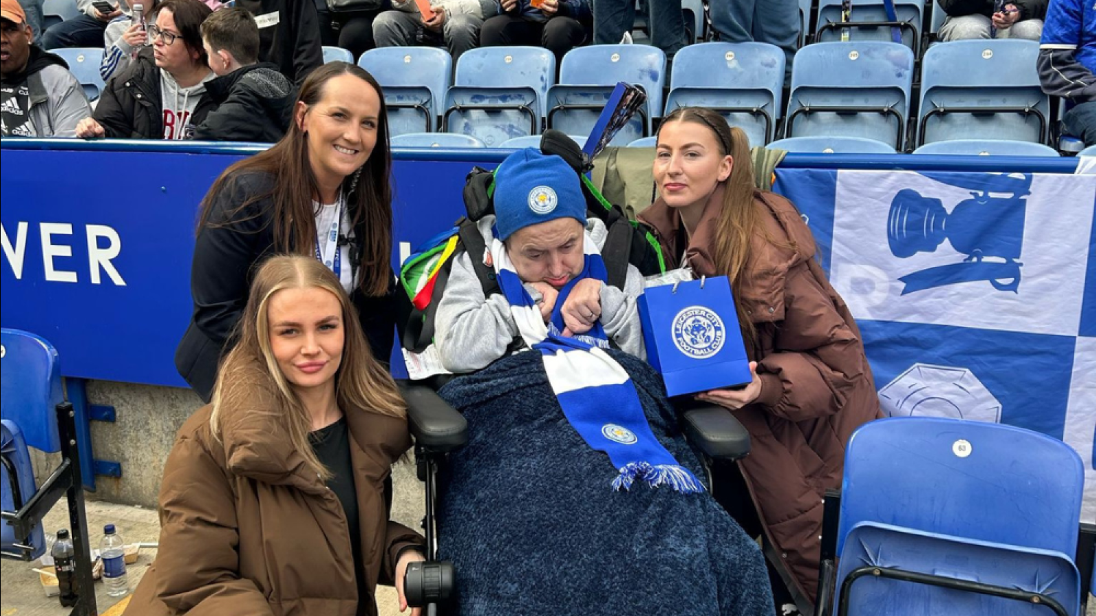 Service user in wheelchair along with three health care workers smiling in a football stadium