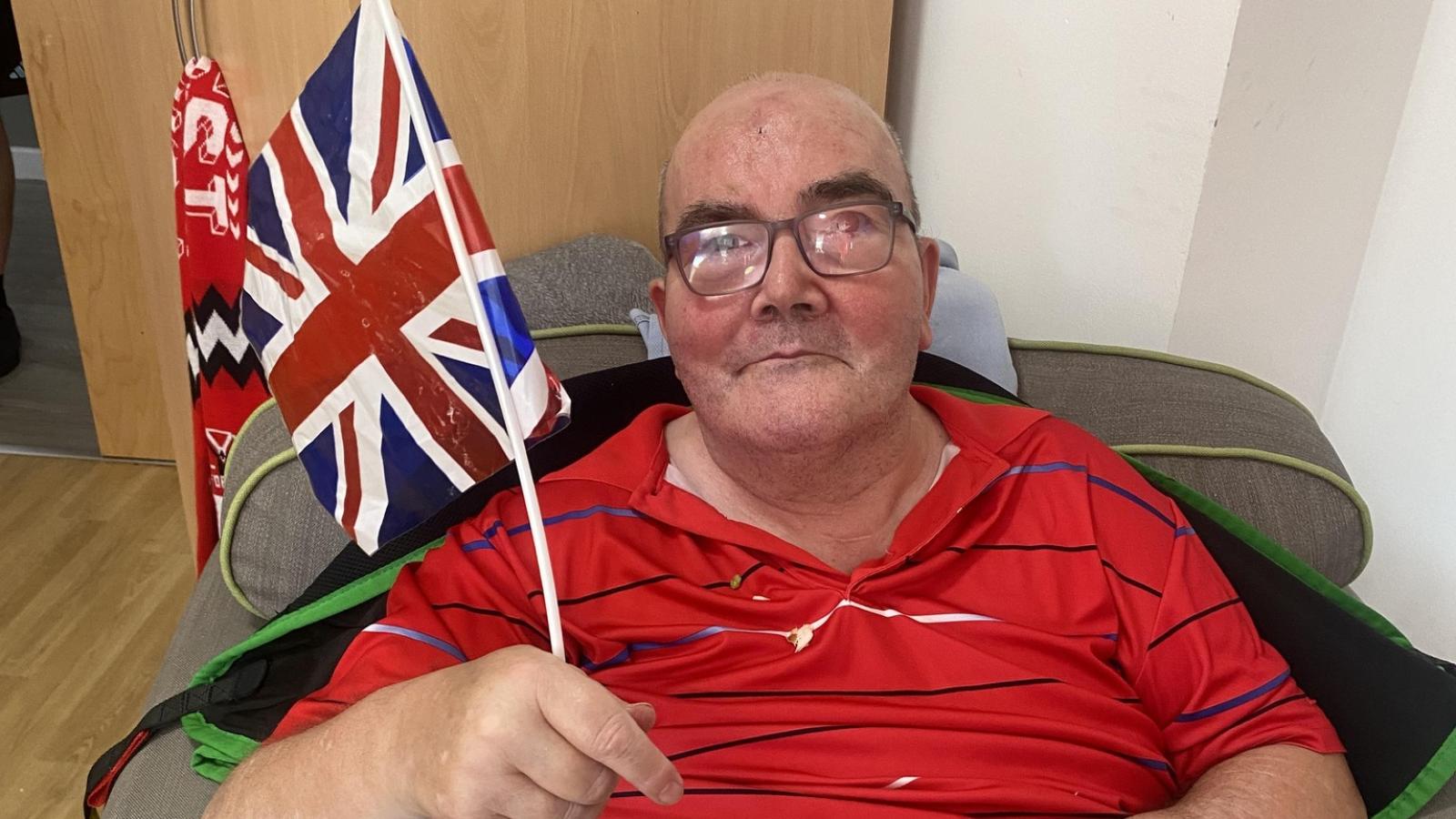 Male sitting down eating fish and chips with Union Jack in hand