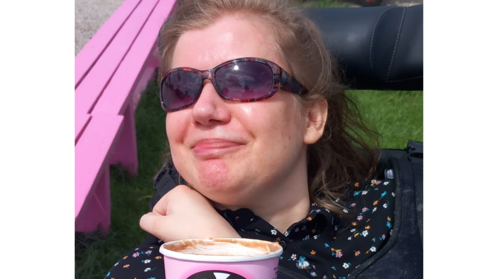 A person with sunglasses on smiling with a hot chocolate