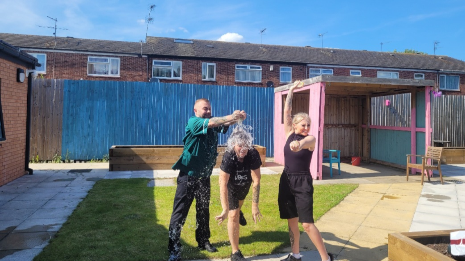 Three people having a waterfight in the garden