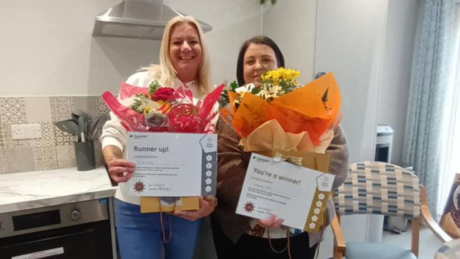 Two people posing for a photo holding certificates and flowers