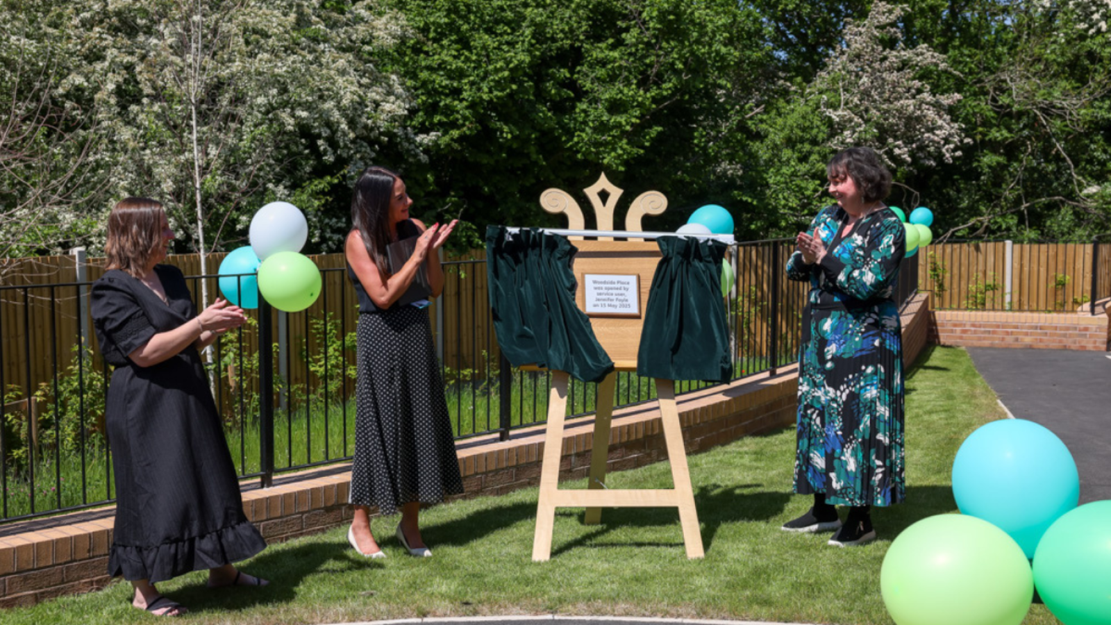 Three people open a curtain on an easel to unveil a plaque 