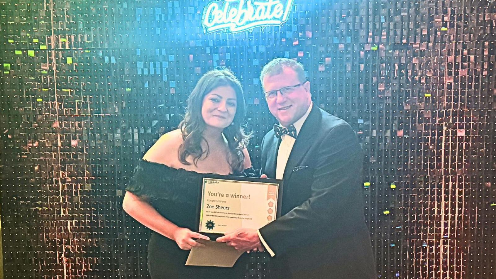 Colleague receiving a certificate and trophy saying 'Values Awards winner' in front of a glittery backdrop 
