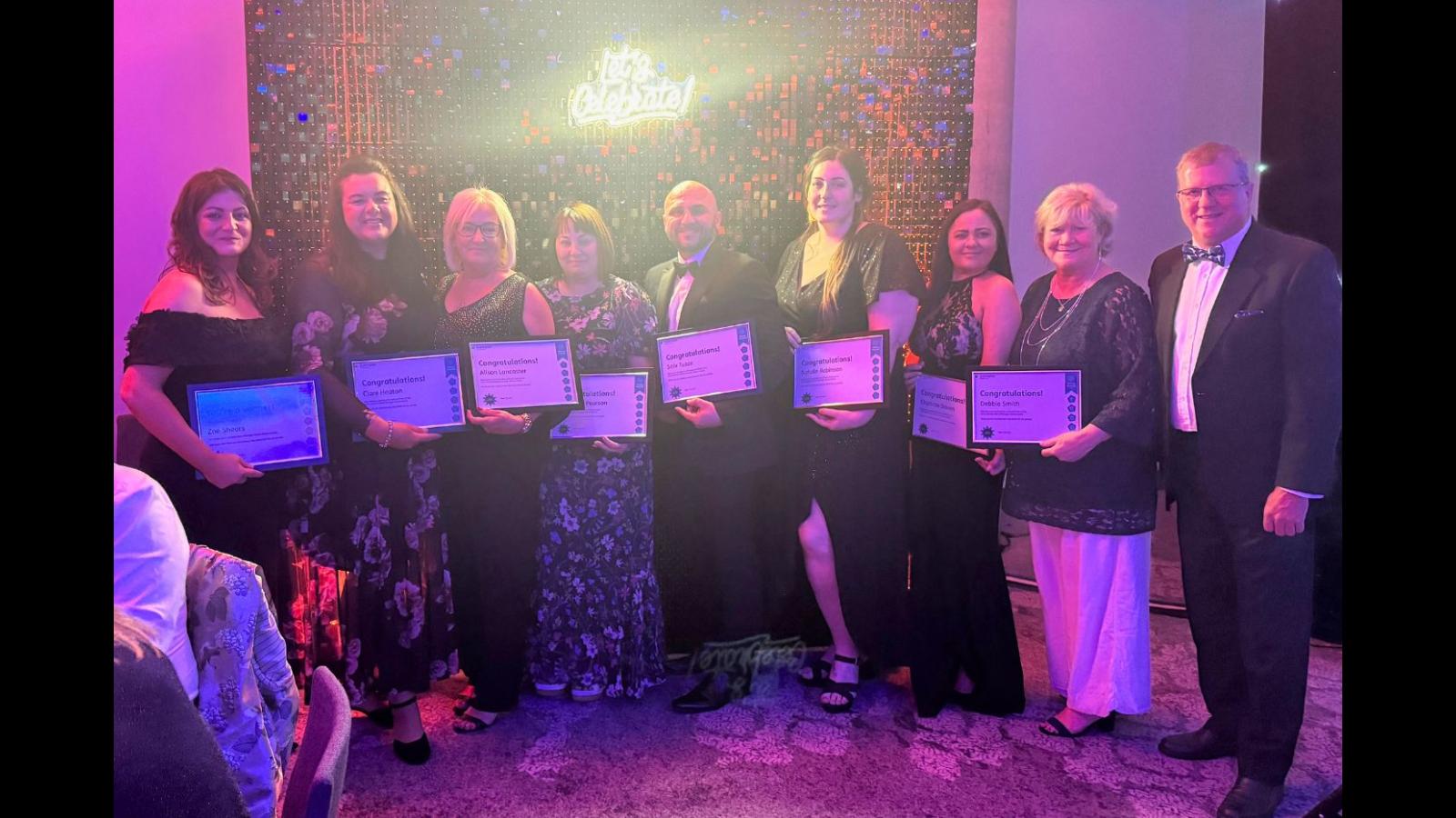 Eight colleagues standing with certificates saying 'Values Awards finalists' in front of a glittery backdrop 