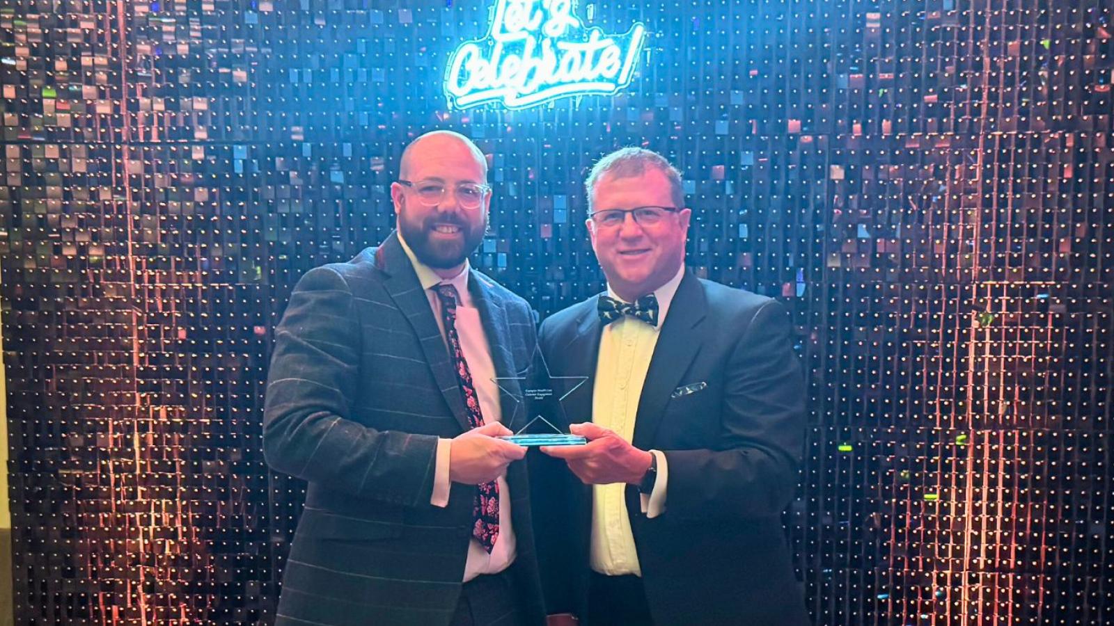 Colleague receiving a trophy in front of a glittery backdrop 