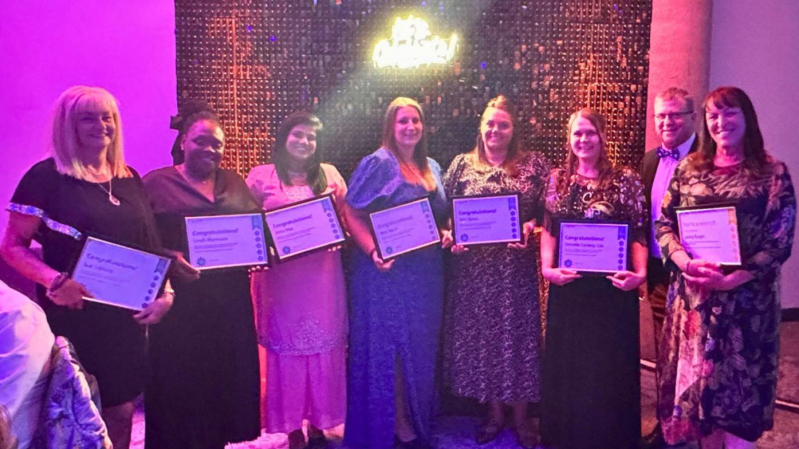 Eight colleagues standing with certificates saying 'Values Awards finalists' in front of a glittery backdrop 