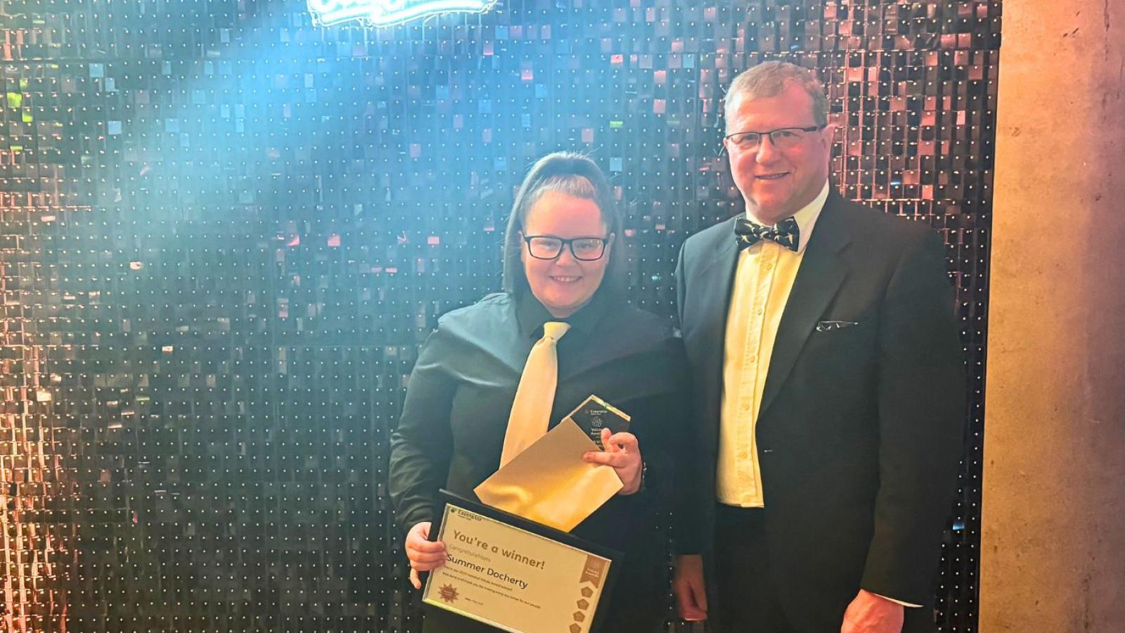 Colleague receiving a trophy in front of a glittery backdrop 
