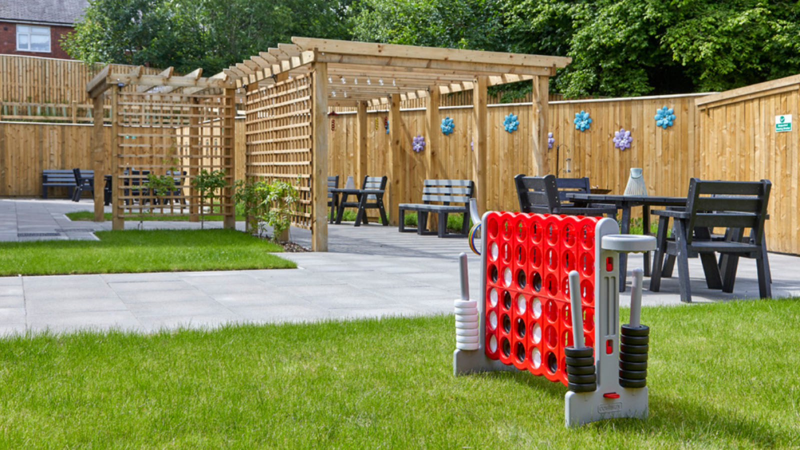 A photo of a garden surrounded by a wooden fence with tables and chairs and a garden game