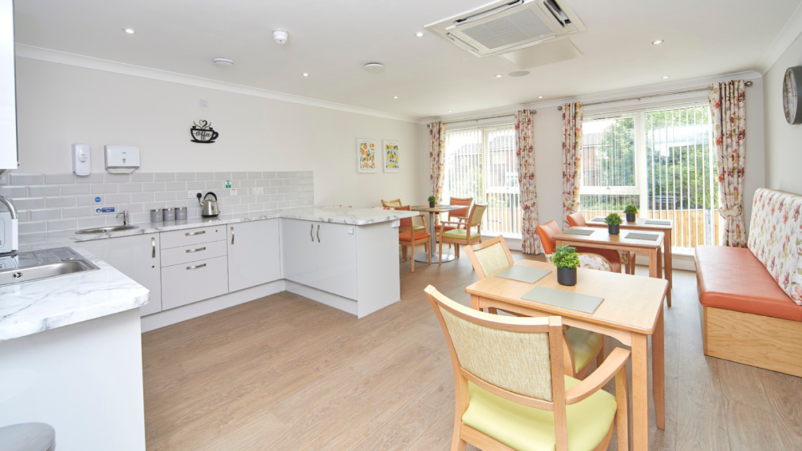 A photo of a kitchen/dining room area with different style tables and chairs throughout the room and two large doors leading out into the garden