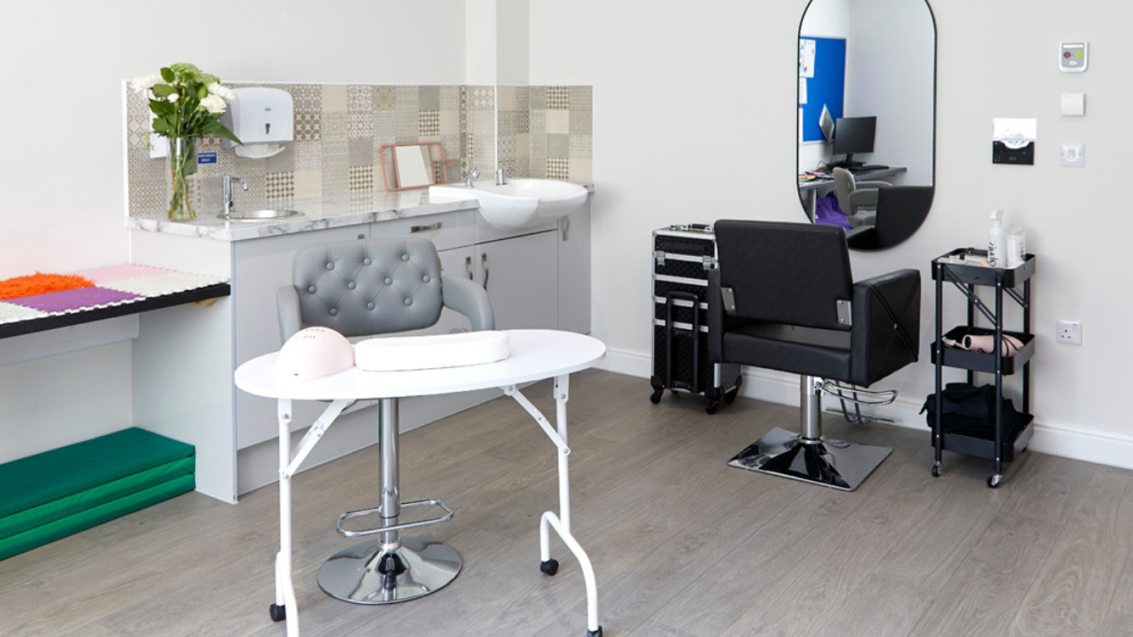 A salon with hairdressing chair facing a mirror on the wall and a table and chair for nails
