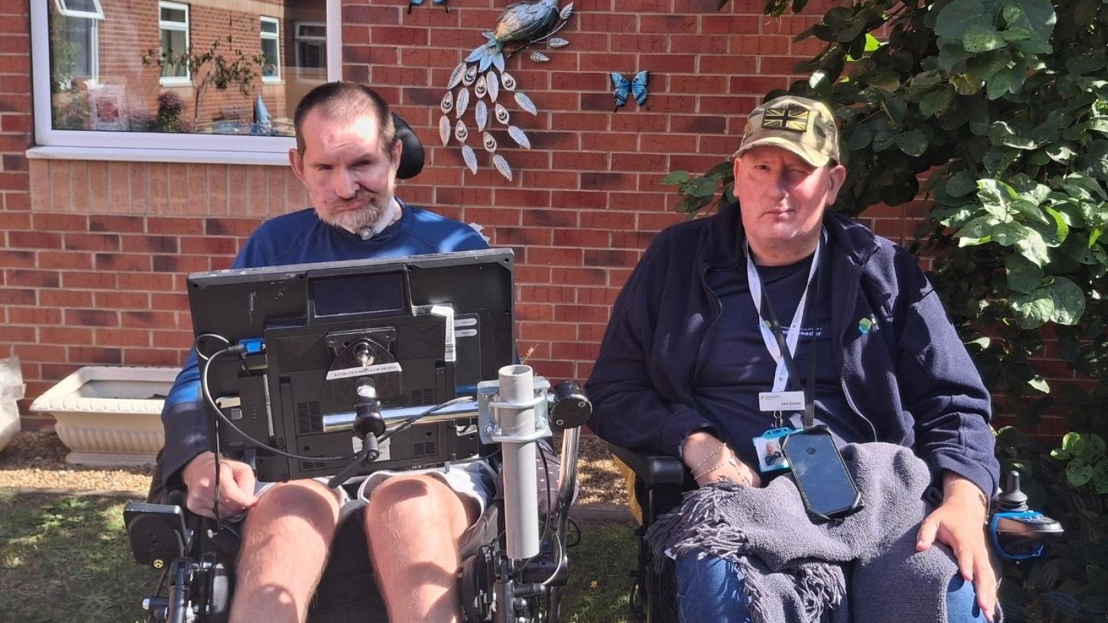 Two males in wheelchairs sitting together in a garden setting