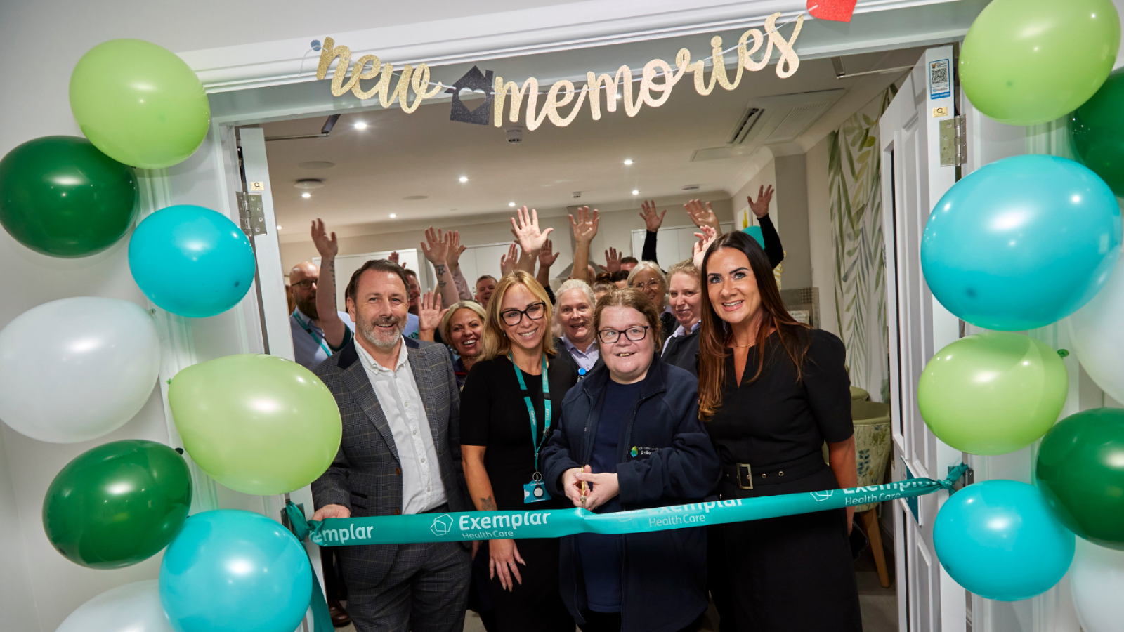 A group of people stand behind a ceremonial ribbon with one person holding gold scissors about to cut