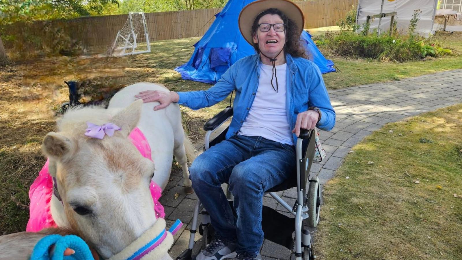Man in a wheelchair dressed in a cowboy outfit with a miniature horse