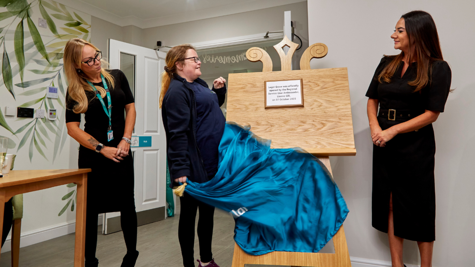 Three people sand beside an easel as a drape is removed to unveil a plaque