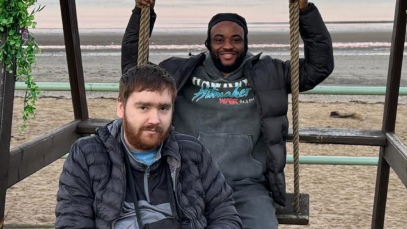 Two individuals enjoying time on swings with a scenic beach backdrop.