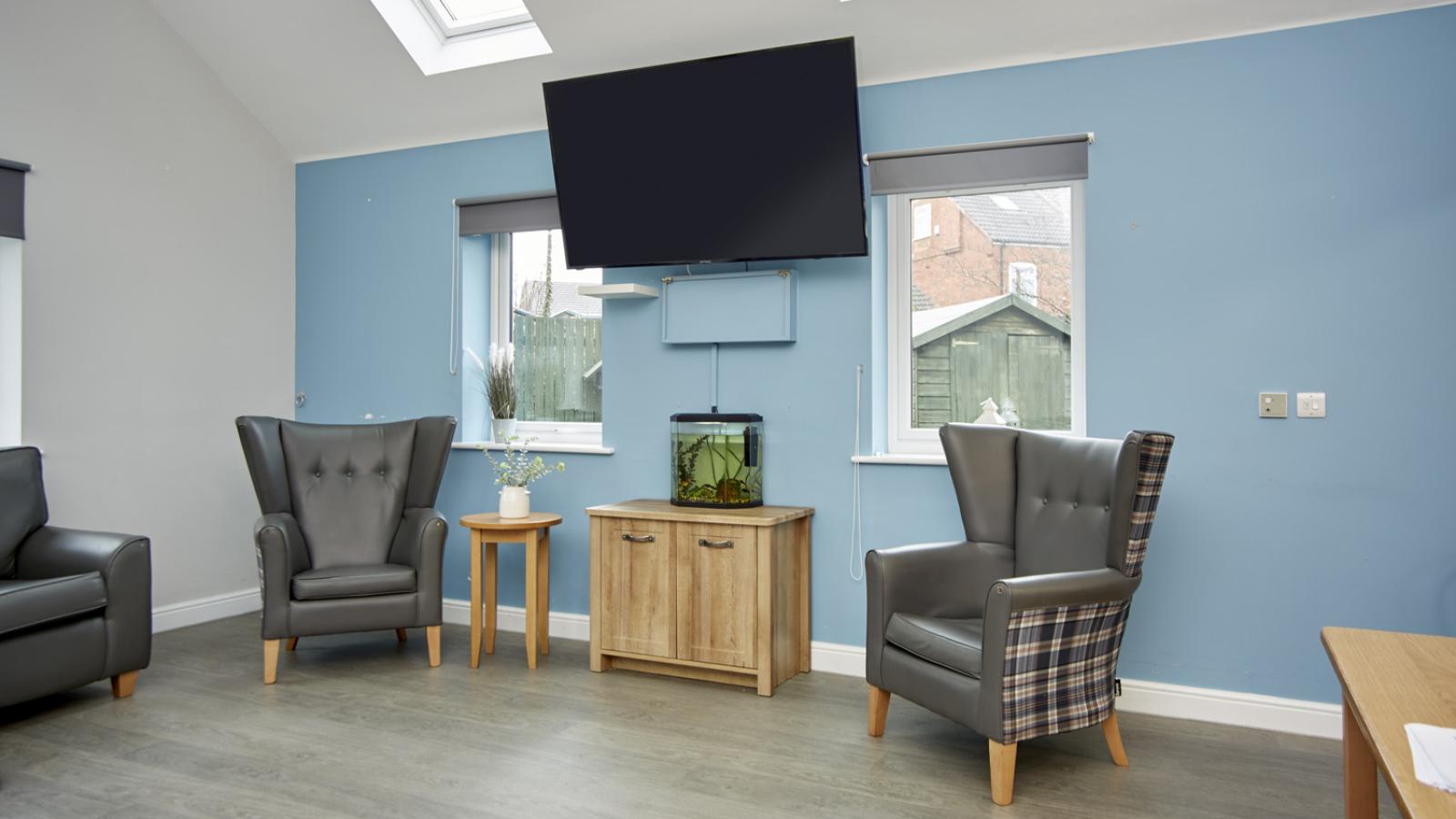 Corner of lounge area with two chairs either side of a TV on the wall