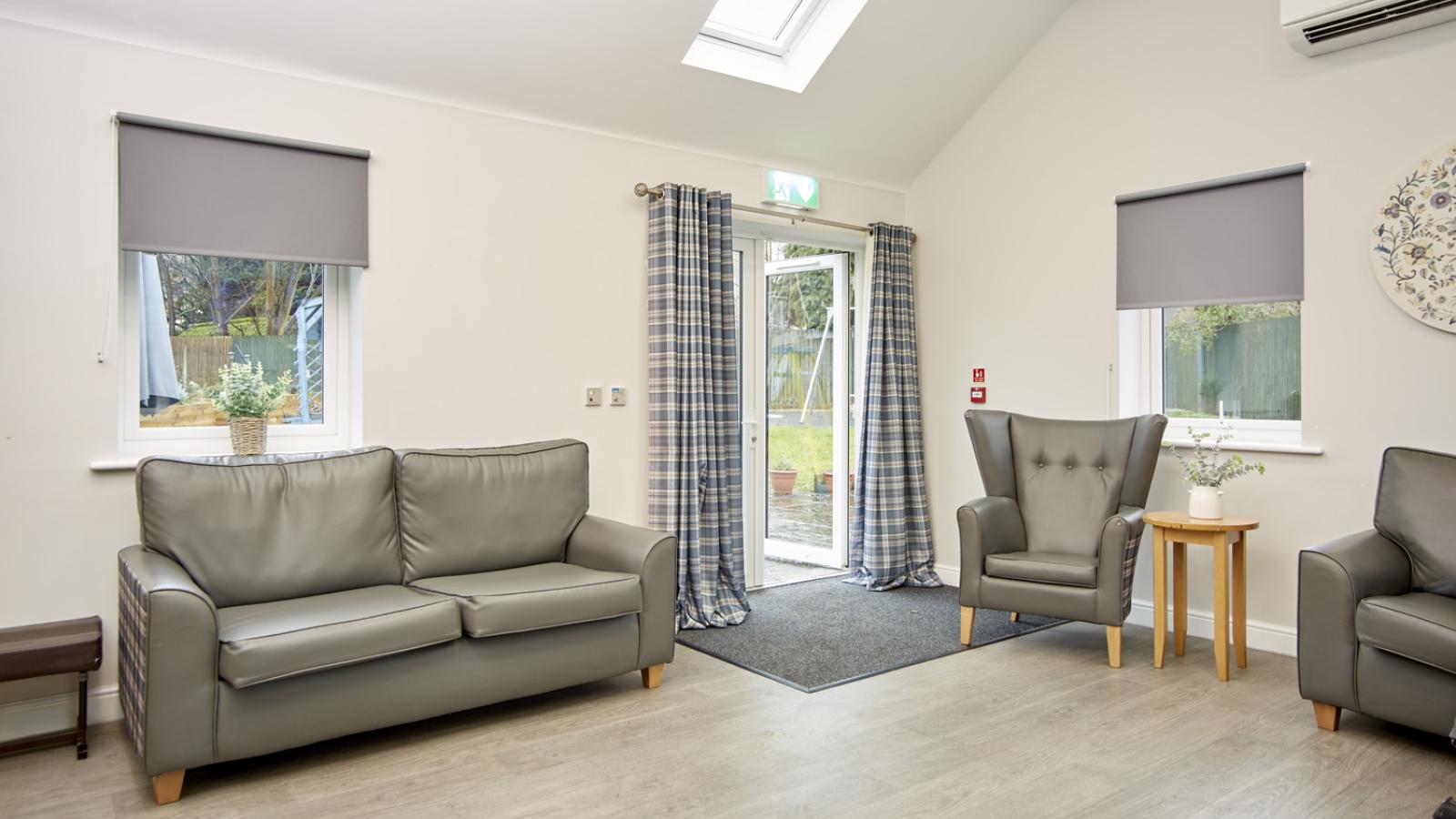 Corner of a lounge with a sofa and chair either side of an open patio door out onto the garden