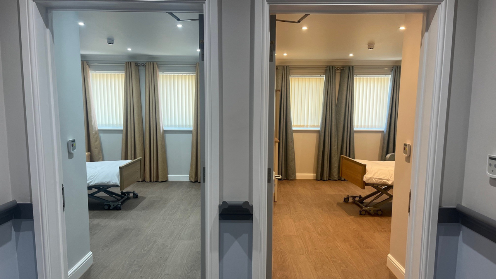 Two adjacent rooms with hospital beds and neutral decor. Each room has wood flooring, beige curtains and blinds, creating a calm and sterile atmosphere.