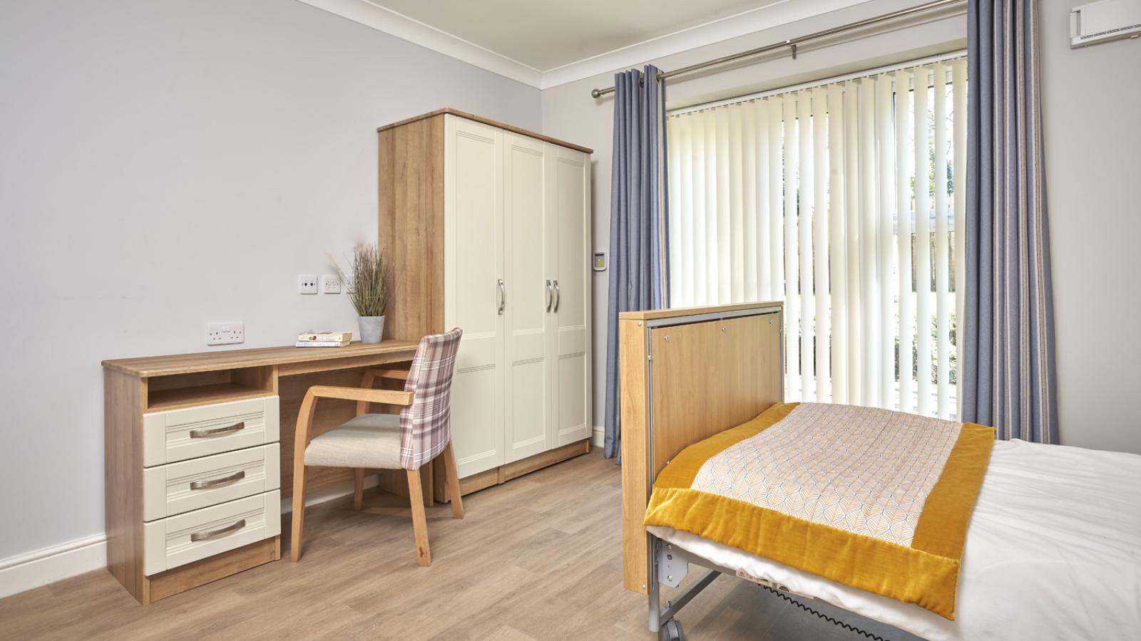 Bedroom setting showing the end of a bed, with a wardrobe and dressing table in the background