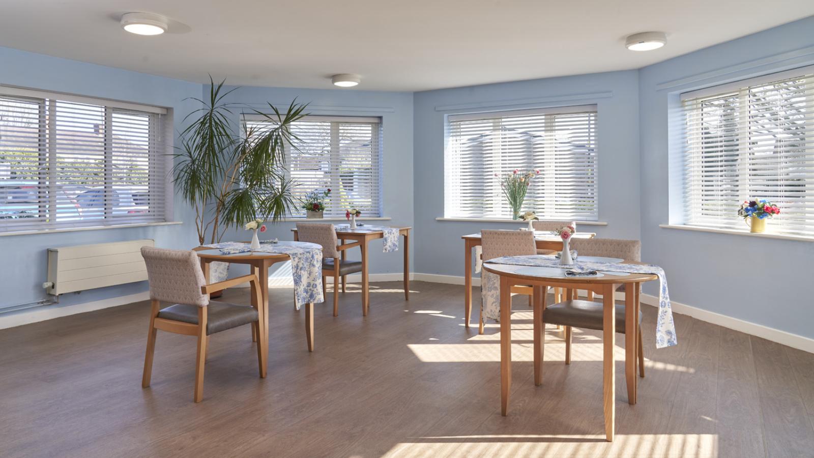 Dining room with blue walls, big windows, and four tables set up