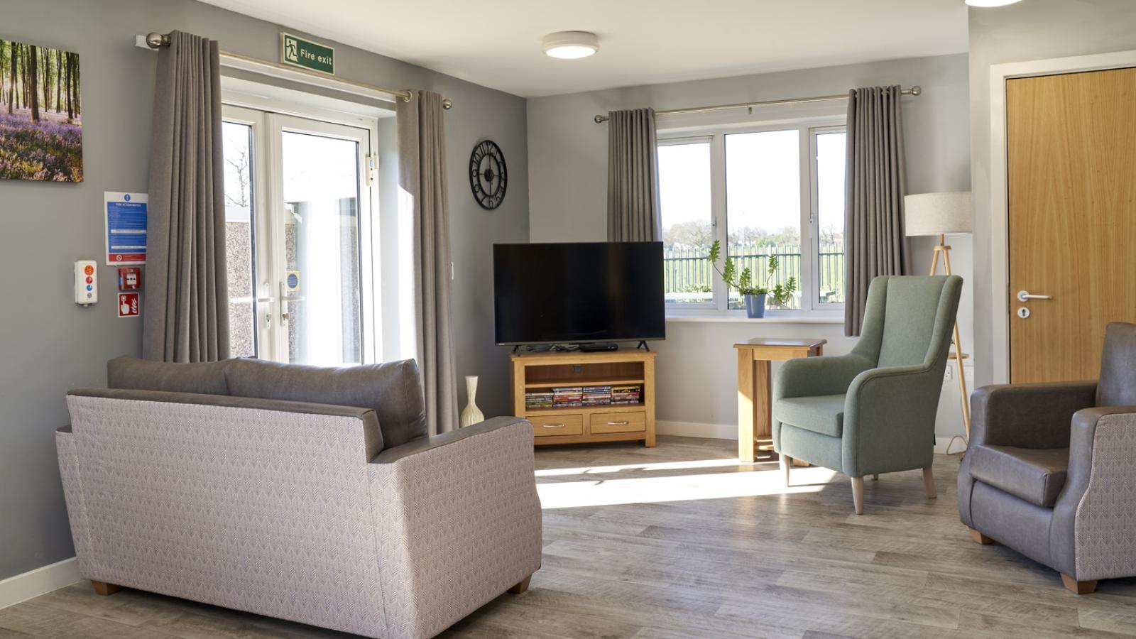 Lounge setting with sofa, chairs, and TV, with two patio doors leading out onto the garden