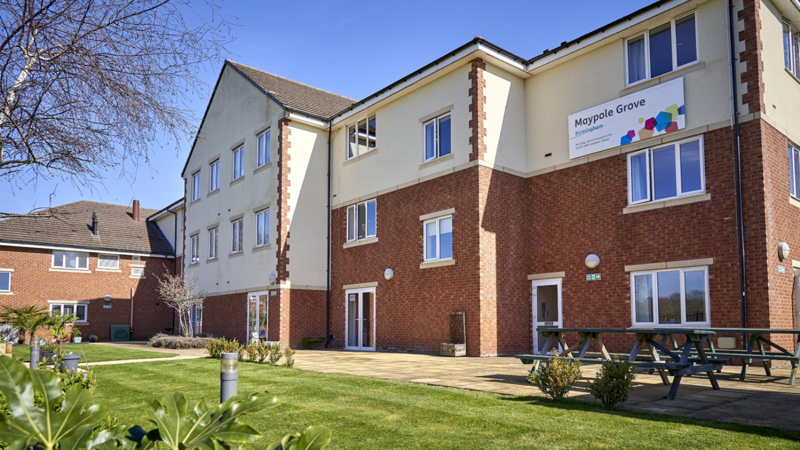 Care home building in background with a green lawn and picnic benches in the foreground