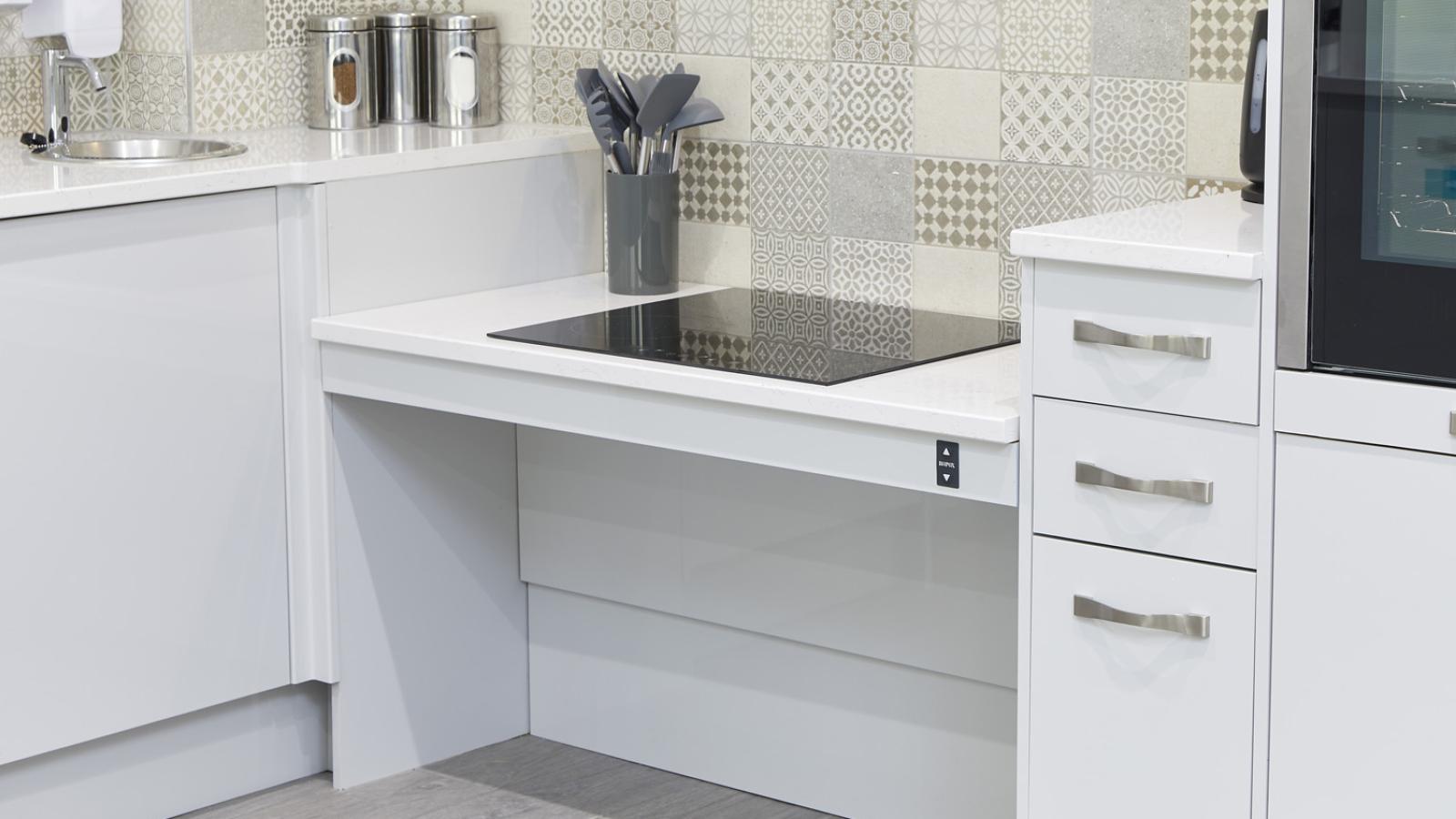 Modern kitchen with a sleek black induction cooktop set into white countertops. Patterned tile backsplash adds a touch of elegance. Stainless steel utensils and containers convey a clean, contemporary feel.