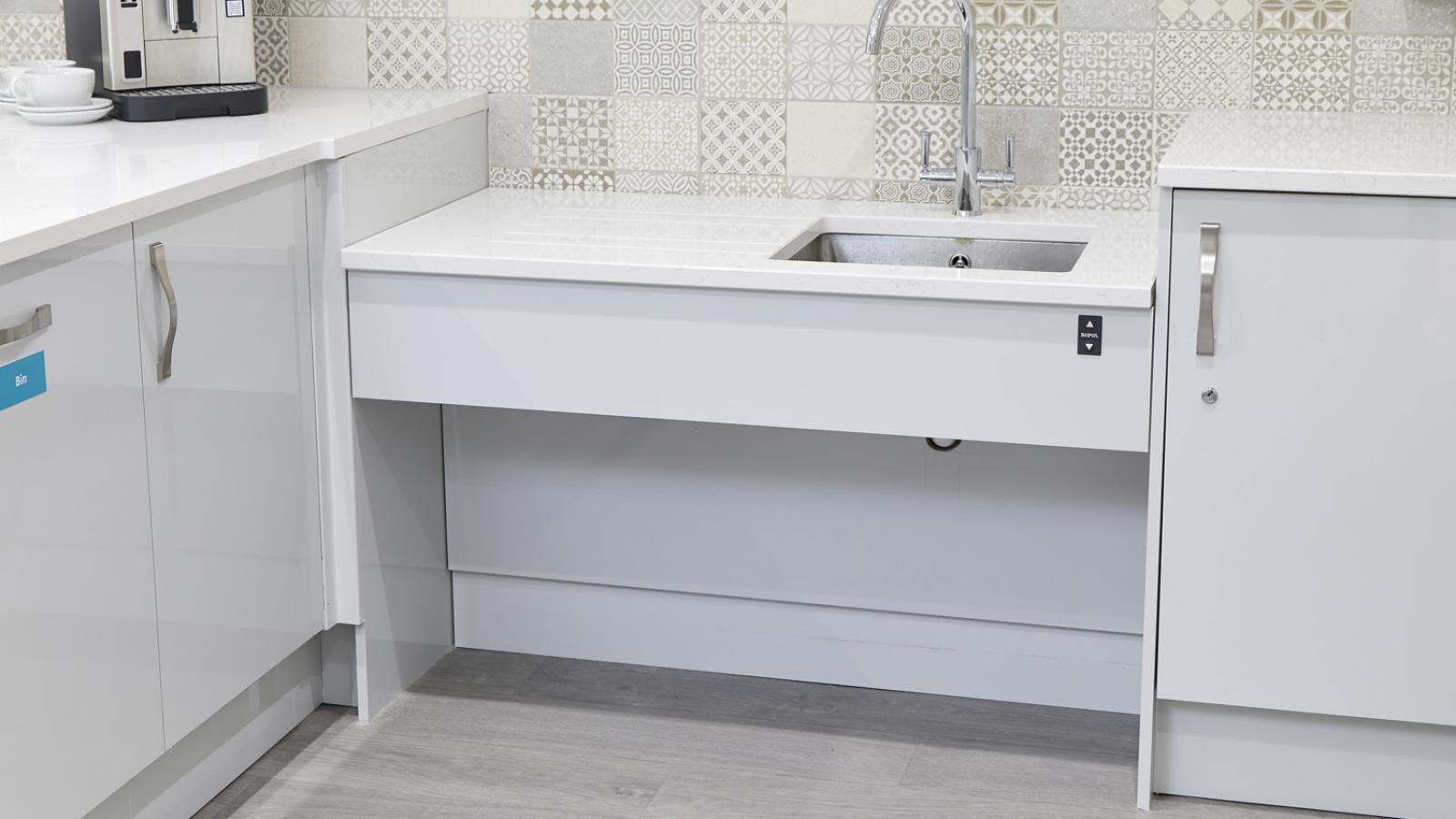 Modern kitchen featuring a patterned tile backsplash, sleek white cabinets, a coffee maker, and a sink with a tall faucet. The tone is clean and contemporary.