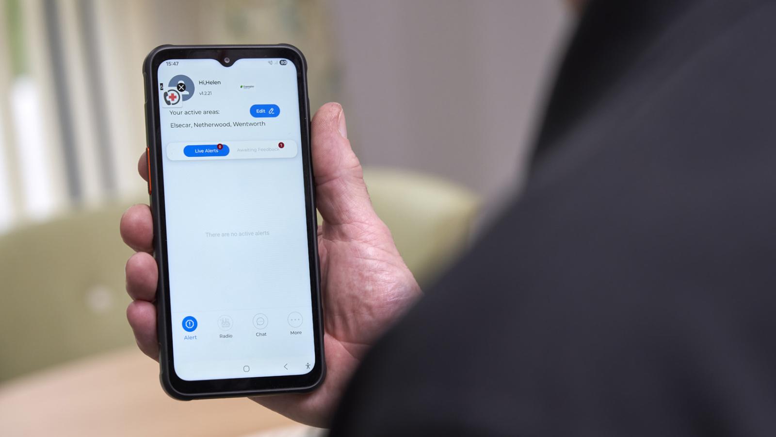 A person holds a smartphone displaying a messaging app screen. The interface shows a conversation with options for alert, pause, chat, and more at the bottom.