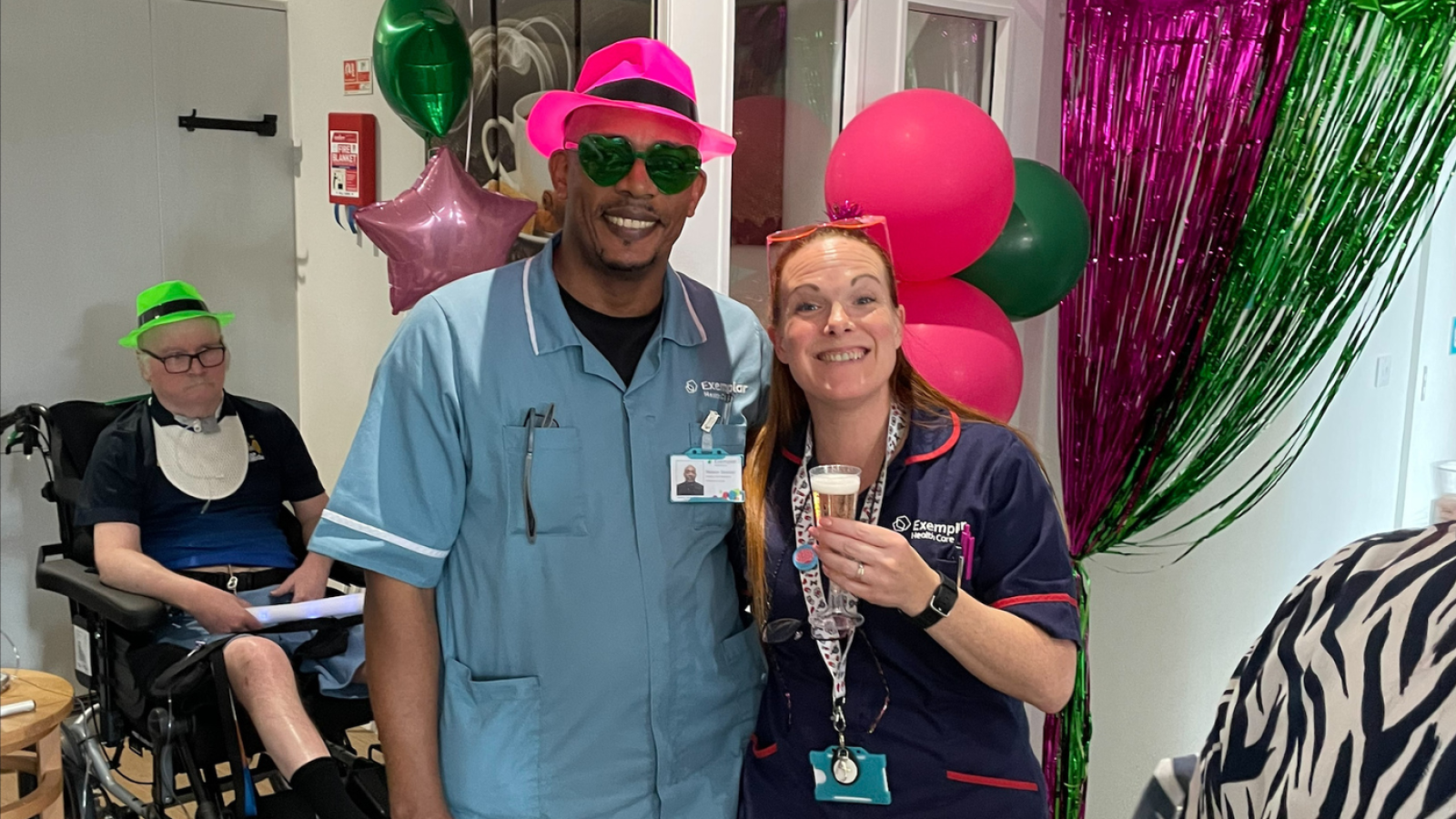 Two people in pink and green costumes cheerfully holding glasses of champagne, celebrating a festive occasion.