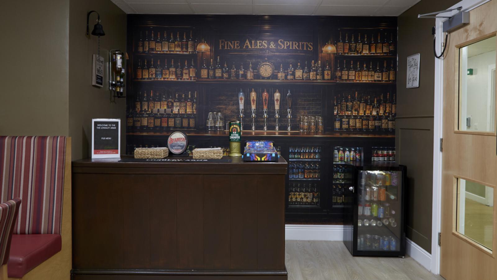 A cozy bar corner with a wooden counter, shelves of fine ales and spirits, and a mini fridge filled with assorted drinks.