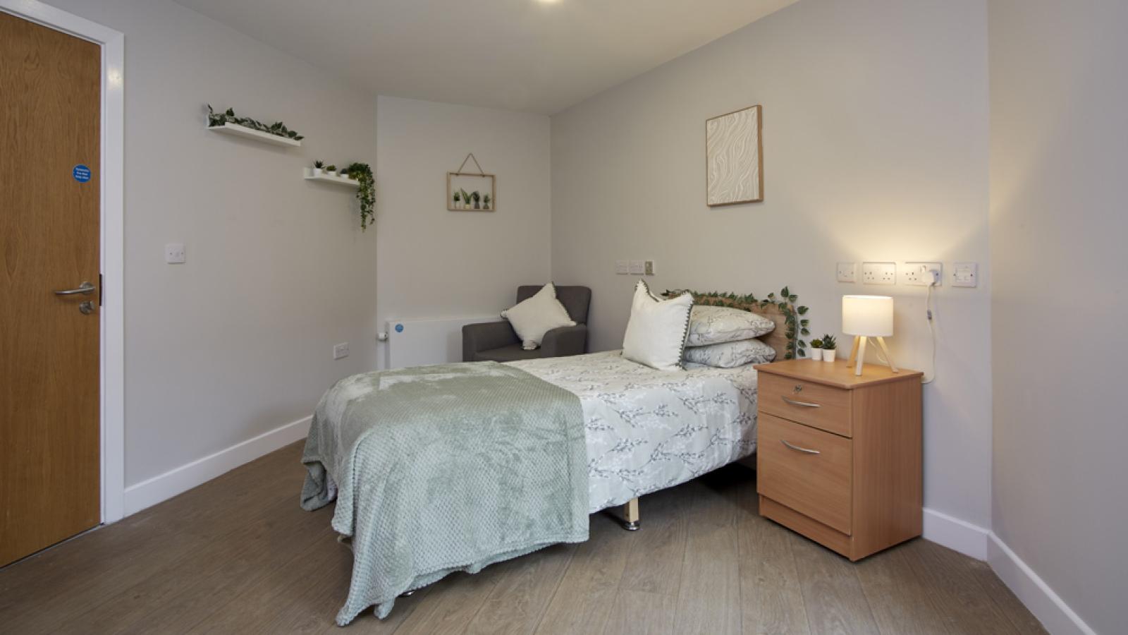 A cozy bedroom with a neatly made bed, wooden nightstand, soft lighting, and wall decor, creating a warm, inviting atmosphere