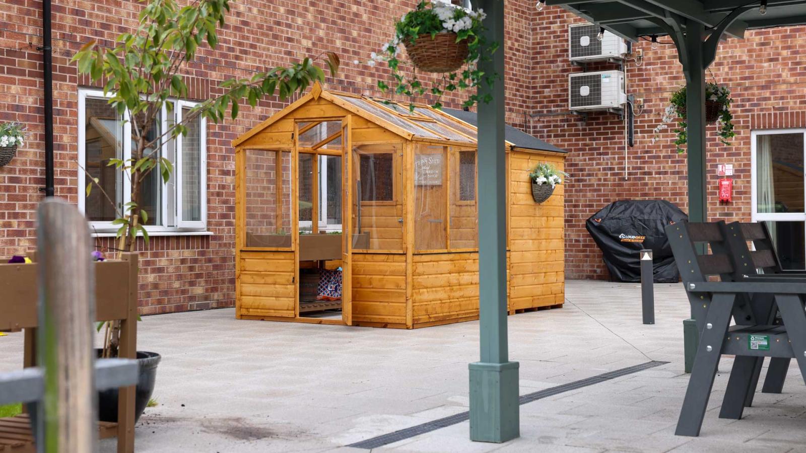 Outdoor garden shed with a greenhouse, set back against an outdoor seating area