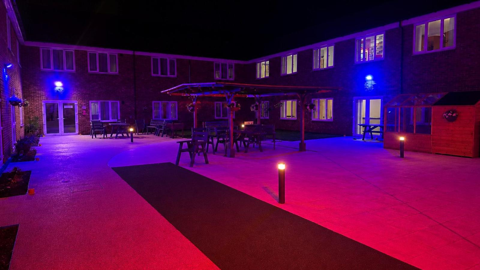 Outdoor courtyard area with patio and grass area, with seating in the middle, with coloured lights around