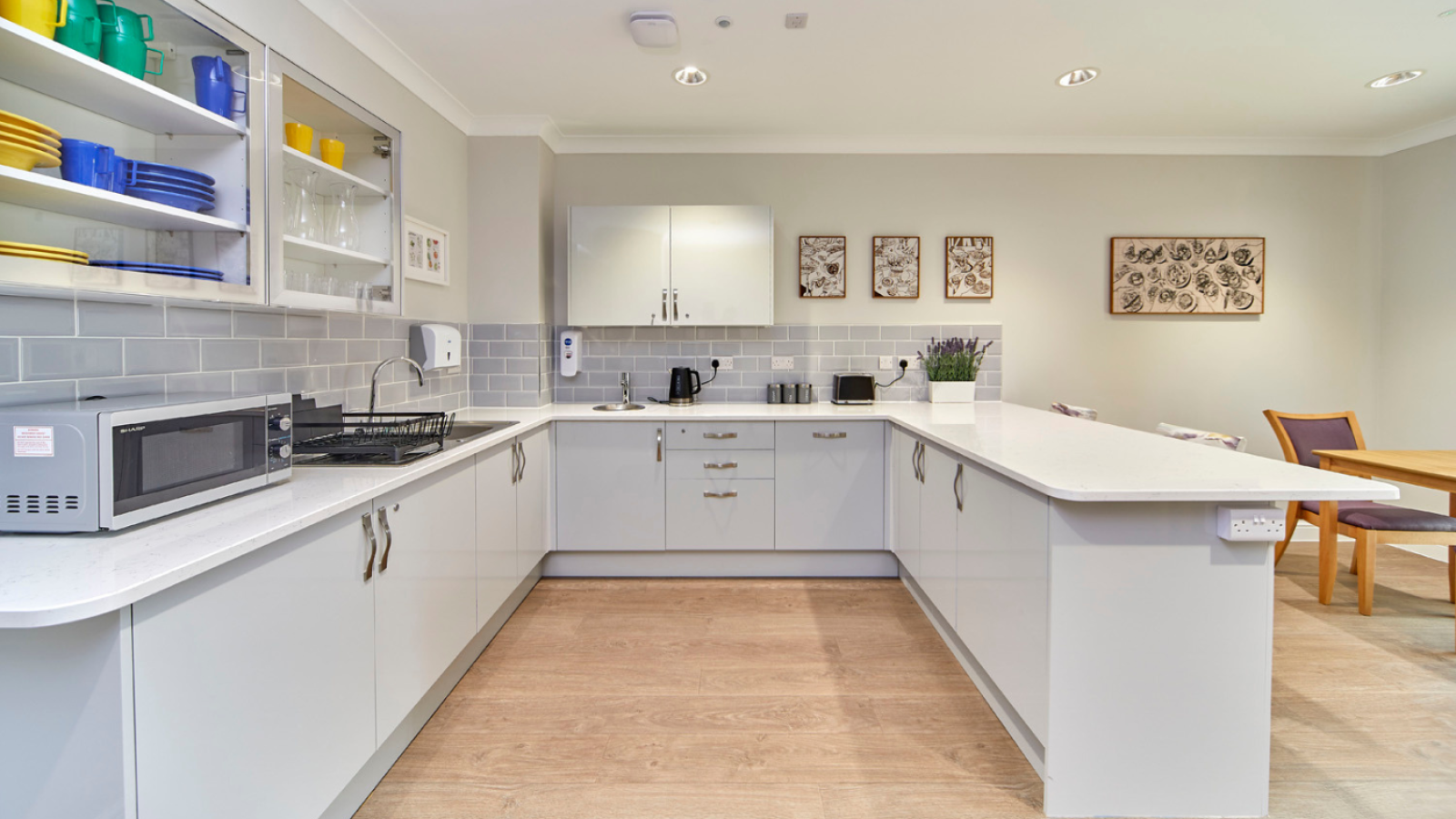 Bright modern white kitchen with gray backsplash, island, wood floors, open shelving, appliances, and dining area; clean, welcoming space.