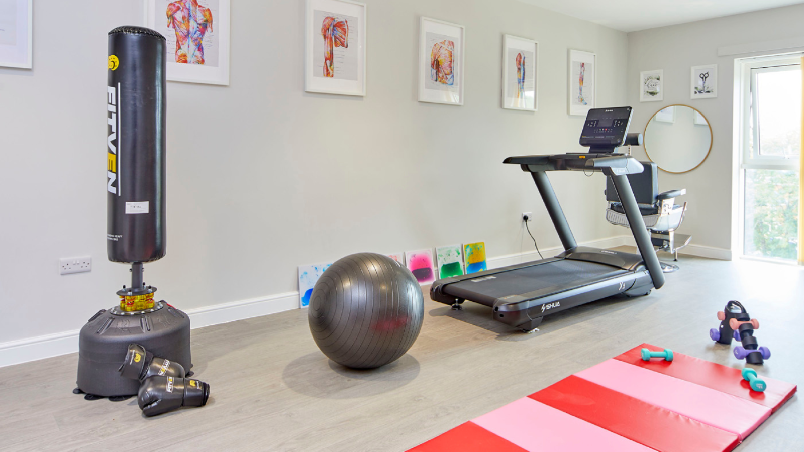 Bright home gym with punching bag, treadmill, exercise ball, yoga mats, dumbbells, and framed art, creating an inviting workout space.